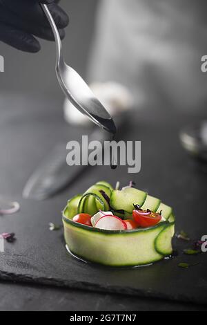 Ein Gemüsesnack aus frischem Gemüse wie Gurken, Tomaten, Feta-Käse und Mikrogemüse. Ein mit einem Giebel geliebte Koch gießt schwarze Sauce über eine Gourmet-DIS Stockfoto