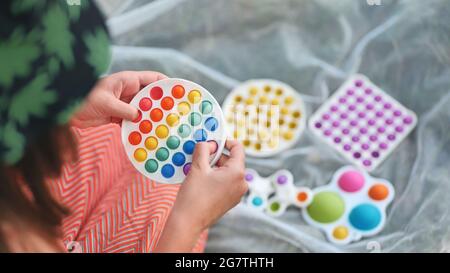 Teenager Mädchen spielt mit Anti-Stress mehrfarbigen Spielzeug popit und einfache Grübchen im Park an einem Sommertag. Stockfoto
