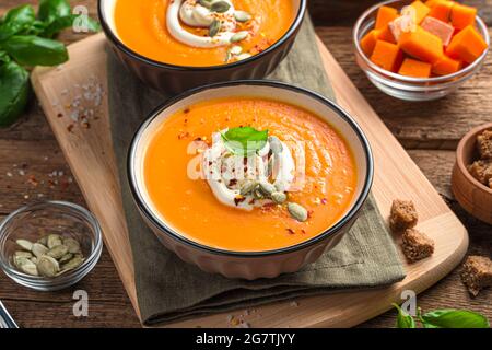 Kürbiscremesuppe mit Creme und Kürbiskernen auf braunem Holzgrund. Stockfoto