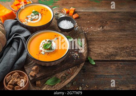 Zwei Tassen Kürbissuppe mit Basilikum und Creme auf Holzboden. Stockfoto