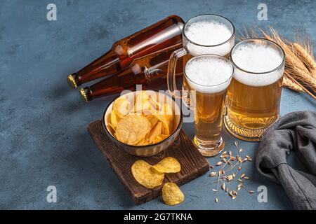 Bierbecher und -Flaschen, Chips und Weizen auf dunklem Hintergrund. Stockfoto