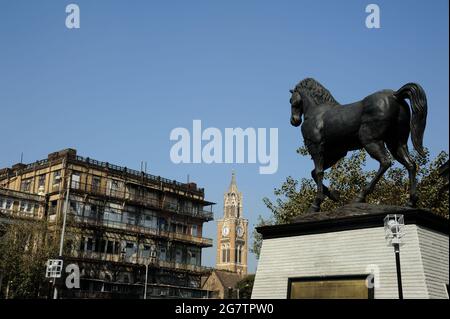 Kala Ghoda die Statue der Bronzeskulptur 25 Fuß Denkmal; hat das Pferd den Namen ‘Geist von Kala Ghoda’. Kultiger Horse Rajabai Uhrenturm im Hintergrund Stockfoto