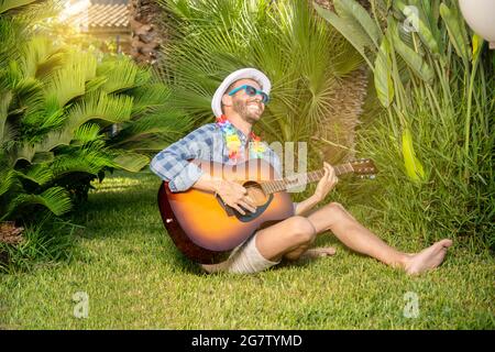 Porträt eines jungen, stilechten spielenden und singenden Mannes mit Gitarre in einem Garten Stockfoto