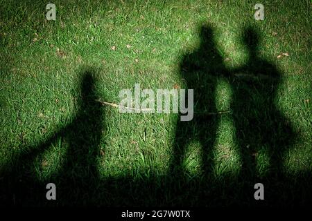 Schatten von drei Menschen werden durch das starke Sonnenlicht auf dem Gras reflektiert Stockfoto