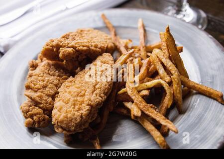 Ein Teller mit Hähnchenbrettieren und dünnen goldenen Pommes Frites Stockfoto