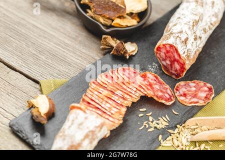 Salami-Wurst in Scheiben mit getrockneten Scheiben von Steinpilzen und Fenchel Herb auf Holzboden. Stockfoto