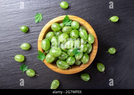 Frische Stachelbeeren in Holzschale auf schwarzem Stein Schiefer Hintergrund. Draufsicht. Stockfoto