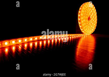 Diode Dekorband für die Beleuchtung, eine Rolle LED-Streifen mit gelbem warmem Licht auf dem Boden Laminat. Stockfoto