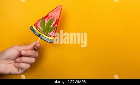 Schöner süßer roter Lollipop mit Marihuana in der Hand auf gelbem Hintergrund, Süßigkeiten mit Cannabis. Stockfoto