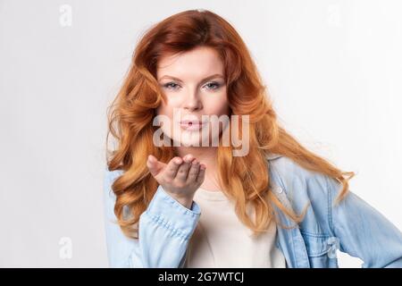 Erwachsene Ingwer Frau mit offenen Handflächen in der Nähe des Mundes senden schönen Kerl Luftkuss. Stockfoto