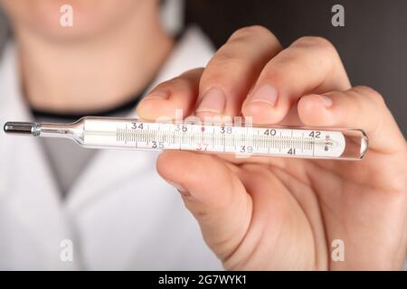 Der Arzt hält ein Quecksilberthermometer in der Hand in Nahaufnahme, Diagnose Coronavirus COVID-19. Stockfoto