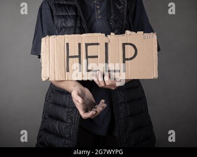 Ein schmutziger Obdachloser steht mit einem Pappschild und bittet um Hilfe. Stockfoto