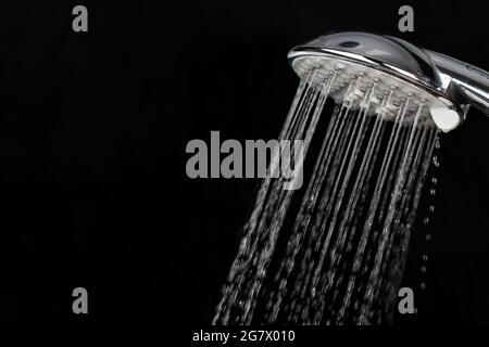 Streuen von Spritzwasser durch einen Duschkopf auf dunklem Grund. Stockfoto