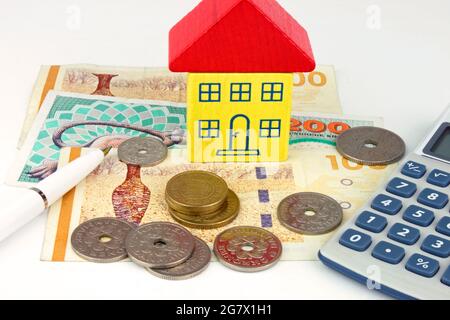 Ein Spielzeughaus, das auf dänischen Kronerscheinen sitzt, mit Münzen und einem Taschenrechner. Ein Foto, das die dänischen Hauskosten und die Finanzierung zeigt. Stockfoto