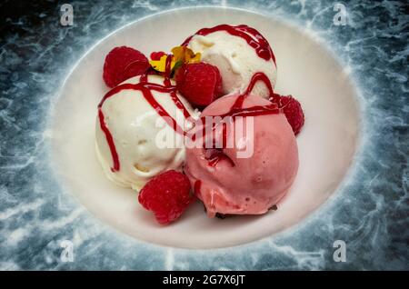 Erdbeer- und Vanilleeis mit Himbeeren und Himbeer-Coulis große blaue und weiße Schale, aus nächster Nähe Stockfoto