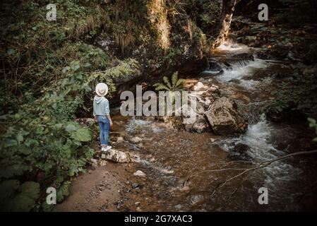 Junge Touristenfrau, die am Bergfluss entlang wandert und die Landschaft genießt. Reisender, der über Felsen läuft. Sommerurlaub. Hochwertige Fotos Stockfoto