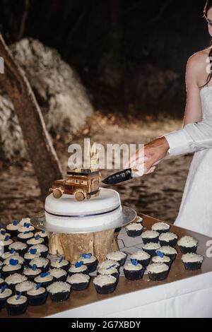 Vertikale Nahaufnahme des Brautpadens beim Schneiden des Hochzeitstortes. Stockfoto