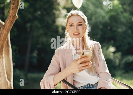 Erfolgreiche junge Geschäftsfrau, die im Café im Freien sitzt und das Smartphone benutzt Stockfoto