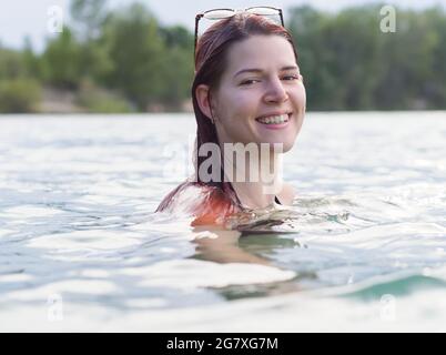 Porträt einer jungen Frau mit roten Haaren beim Schwimmen im See Stockfoto