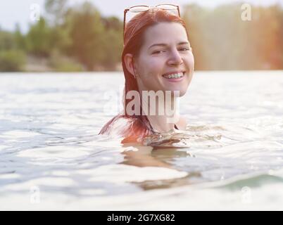 Porträt einer jungen Frau mit roten Haaren beim Schwimmen im See Stockfoto