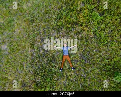 Luftaufnahme von einer Drohne eines Mannes, der in hohem Gras auf dem Rücken liegt Stockfoto