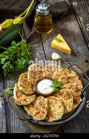 Gesunde Sommernahrung, Zucchini-Krapfen. Vegetarische Zucchini-Pfannkuchen mit Käse, serviert mit Sauerrahm auf einem rustikalen Holztisch. Stockfoto