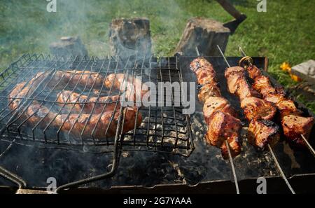 Grillen Sie Fleisch und Würstchen oder Bratwurst auf einem Grillrost im Hinterhof. Mann, der Schaschlik oder Schischkebab über Holzkohle vorbereitet. Gegrilltes Fleisch auf Metall Stockfoto