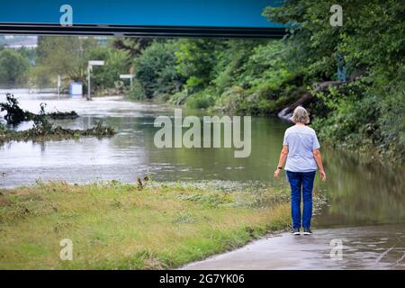 Hattingen, NRW, Deutschland. Juli 2021. Eine Frau geht auf einem normalerweise beliebten Pfad entlang des Flusses, der jetzt im Wasser untergetaucht ist. Die Ruhr hat ihre Böschung, Felder und viele Gärten, Keller und Grundstücke in der Nähe der Stadt Hattingen im Ruhrgebiet in Nordrhein-Westfalen überflutet. NRW ist nach starken Regenfällen in den letzten Tagen von schrecklichen Überschwemmungen heimgesucht worden. Bei den Überschwemmungen in Deutschland sind bisher mehr als 80 Menschen ums Leben gekommen. Kredit: Imageplotter/Alamy Live Nachrichten Stockfoto