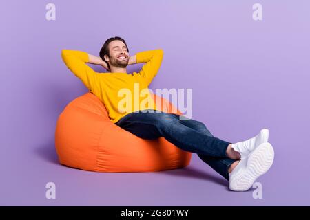 In voller Länge Körpergröße Foto lächelnd Mann lag in Sitzsack entspannend isoliert pastelllila Farbe Hintergrund Stockfoto