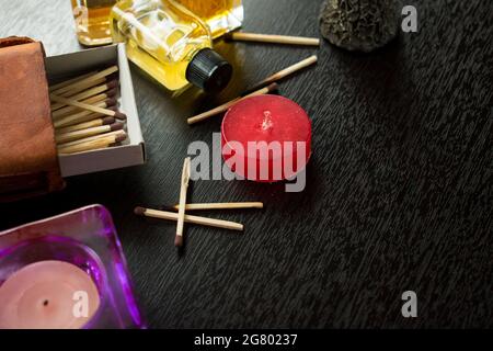 Einige Holzmatches in einer Streichholzkiste, Kerzen und einige Glasflaschen auf einem schwarzen Holztisch Stockfoto