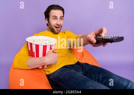 Porträt von attraktiven erstaunt fröhlichen Mann mit Spaß essen Mais beobachten tv-Serie isoliert über pastellviolett lila Farbe Hintergrund Stockfoto