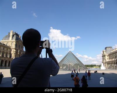 PARIS, FRANKREICH - 10. Aug 2010: Ein Tourist, der ein Foto vom Louvre und der Louvre-Pyramide in Paris, Frankreich macht. Stockfoto