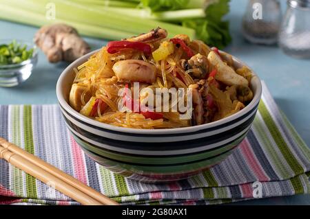Reisnudeln Funchoza mit Meeresfrüchten. Cellophan Pasta, Muscheln, Tintenfisch und Tintenfisch, gesunde asiatische Mahlzeit Snack in einer Schüssel auf hellblauem Hintergrund. Schließen Stockfoto