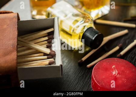 Einige Holzmatches in einer Streichholzkiste, Kerzen und einige Glasflaschen auf einem schwarzen Holztisch Stockfoto