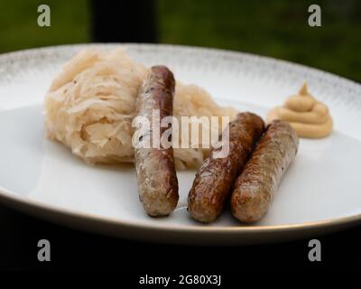 Nürnberger Grillwurst oder Nürnberger Rostbratwurst mit Sauerkraut oder saurem Kohl und Senf auf weißem Teller, Seitenansicht Stockfoto