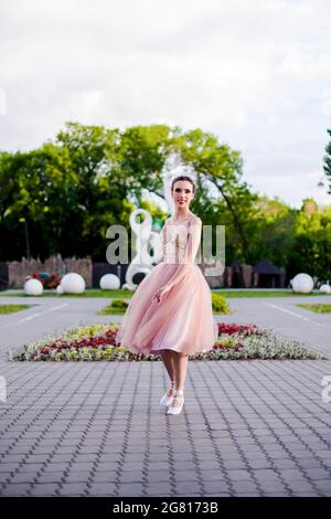 Eine Ballerina in einem langen rosa Seidenkleid dreht sich im Sommer im Park in einem Tanz, Ballett in der Stadtlandschaft Stockfoto