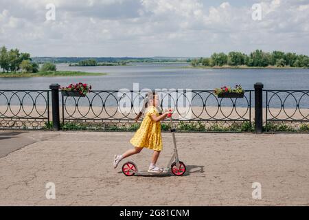 Ein Kind fährt schnell einen Roller entlang der Uferpromenade entlang der Bucht, Spaß an einem Familienwochenende, Aktivitäten für Kinder Stockfoto