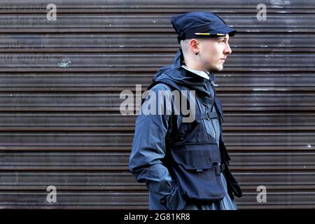 Ein Mann in Seitenansicht, gekleidet in einem unverwechselbaren urbanen Straßenstil vor einem dunklen, metallischen Rolltorhintergrund - Frankreich Stockfoto
