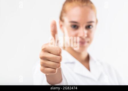 Erfolgreiche junge Frau, die mit einem Daumen nach oben Geste der Exzellenz, Zustimmung, Sieg, Unterstützung oder ein Ja über einen weißen Hintergrund mit Fokus auf ihr h Stockfoto