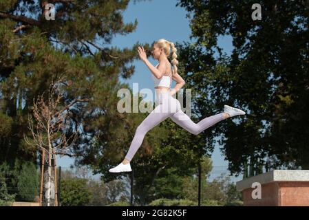 Gesunde und fit atraktive blonde Frau springt nach links über Hindernisse im Park und freut sich nach vorne. Stockfoto