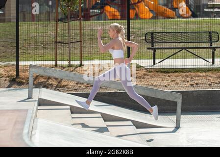 Gesunde und fit atraktive blonde Frau, die eine kurze Betontreppe im Park hochspringt. Stockfoto