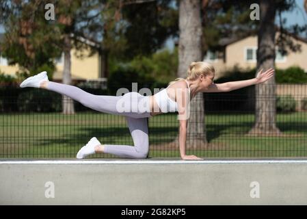 Gesund und fit atraktive blonde Frau zeigt Konzentration und Balance mit Blick nach rechts auf einem Knie im Park. Stockfoto