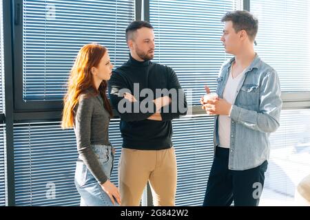 Porträt von drei ernsthaften jungen Geschäftsleuten, die während der Kaffeepause in einem modernen Büro Spaß beim Gespräch haben. Stockfoto