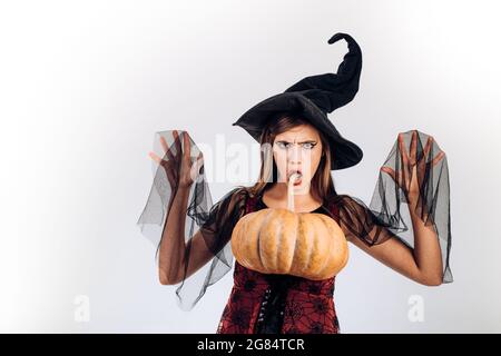 Überraschte Frau. Frau posiert mit Kürbis. Schöne junge überraschte Frau in Hexenhut und Kostüm mit Kürbis. Glückliche Menschen. Stockfoto