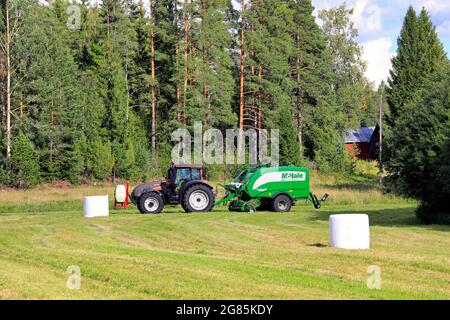 Landwirt, der im Heufeld mit dem Traktor Valtra und dem integrierten Pressenwickler McHale 3 arbeitet. Salo, Finnland. 28. August 2020. Stockfoto