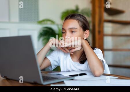 Nahaufnahme eines Teenagers vor einem Laptop. Sie hört sich eine langweilige Online-Lektion an oder macht ihre Hausaufgaben. Konzept des Online-Lernens und Stockfoto