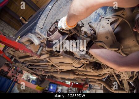 Mit Handschuhen geratende männliche Hände montieren oder entfernen den Bremssattel am Rad eines alten Autos. In der Garage wechselt ein Mann Teile an einem Fahrzeug. Konzept für kleine Unternehmen, Reparatur- und Wartungsservice für Fahrzeuge. UHD 4K. Stockfoto