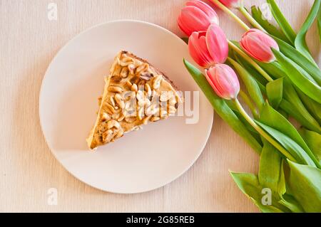 Leckerer Käsekuchen mit karmel und Erdnüssen mit einigen Tulpen im Hintergrund Stockfoto