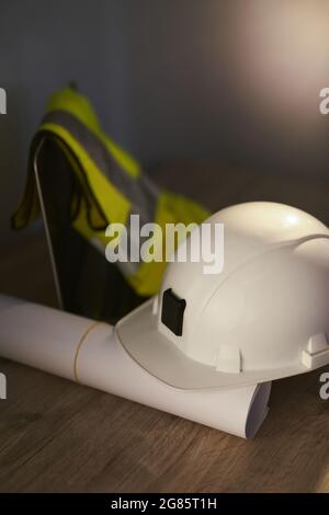 Architect Table Konzept: Weißer Schutzhelm, gerollte Blaupausen, Laptop-Computer und reflektierende Schutzweste. Bau-, Design-, Architektur- oder Bauindustriekonzept. Hochwertige Fotos Stockfoto