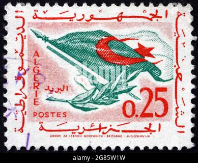 ALGERIEN - UM 1963: Eine in Algerien gedruckte Marke zeigt Flagge, Gewehr und Olivenzweig, um 1963 Stockfoto